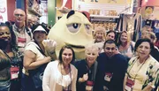 A group of smiling people are posing with a giant M&M character at what appears to be a themed store or event.