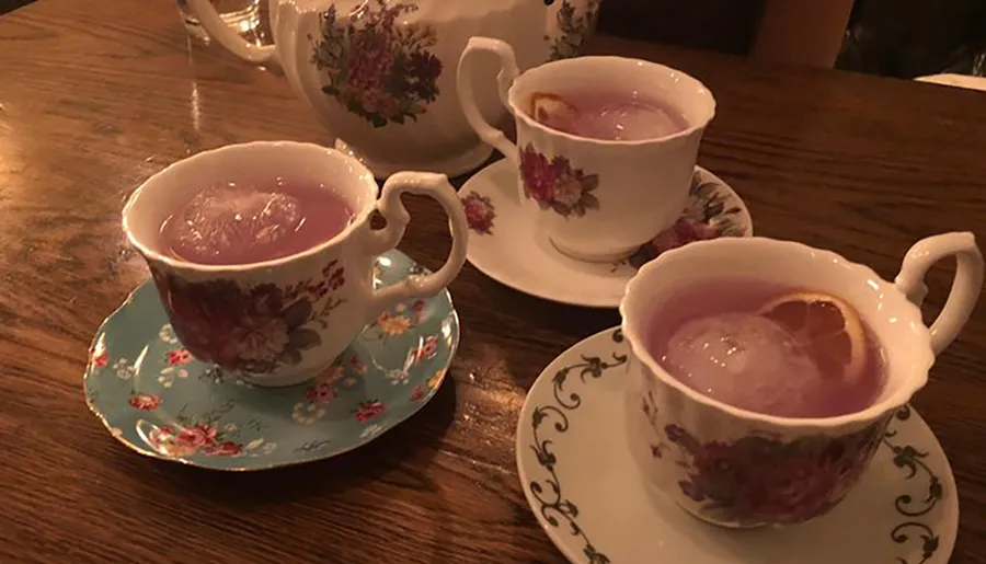 Three vintage floral teacups on saucers are filled with a purple liquid and large spherical ice cubes, suggesting a creative twist on serving cocktails.