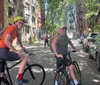 Two cyclists are smiling for the camera on a tree-lined urban street