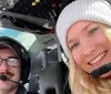 A man and a woman in aviation headsets are taking a selfie inside the cockpit of an aircraft both smiling at the camera