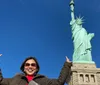 A person is posing with their hands up appearing to mimic the stance of the Statue of Liberty which is prominently featured in the background under a clear blue sky