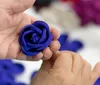 A person is holding a blue fabric rose in their hand against a blurred background of colorful materials