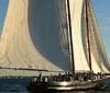 A large sailboat is gliding over the water filled with passengers enjoying a sunny day at sea