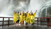 A group of people wearing yellow rain ponchos are cheerfully posing in front of a powerful, misty waterfall.