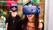 Two people are wearing VR headsets and appear to be delighted by their immersive virtual reality experience.