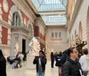 Visitors explore an art gallery featuring classical sculptures and architectural designs with natural light coming in from a glass ceiling