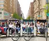 A row of pedicabs each with passengers lines up in front of a picturesque park backdrop with tall buildings in the distance