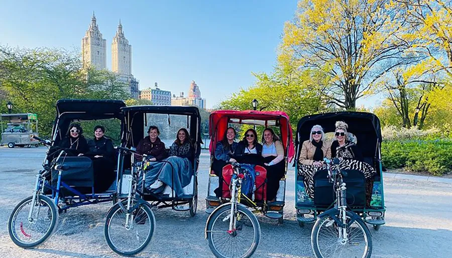 A group of people are enjoying a ride on pedicabs with a backdrop of trees and tall buildings that could be in an urban park.