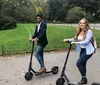 Two people are riding electric scooters along a path with greenery in the background