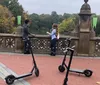 Two people are riding electric scooters along a path with greenery in the background