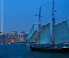 A sailboat with its sails unfurled glides on the water in the evening with the New York City skyline and the Tribute in Light in the background