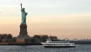 A ferry sails past the Statue of Liberty during what appears to be dusk or dawn.