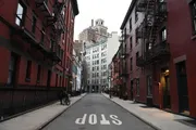 The photo captures a quiet urban street flanked by red brick buildings with fire escapes, leading up to a taller building at the end, with the word 