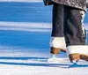 A group of people is enjoying their time on an ice skating rink with a smiling woman in the foreground showing off her balance while another person appears to be bending down or falling in the foreground