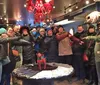 A group of smiling people are holding hands in a line while posing for a photo inside a cozy shop decorated with winter-themed items and a chandelier