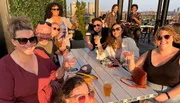 A group of people are enjoying drinks and smiling at a rooftop bar during sunset.