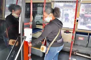 A person is using a hand sanitizer dispenser on a public bus while wearing a face mask.