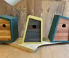 The image shows three wooden birdhouses with different color accents set against a rustic wooden background