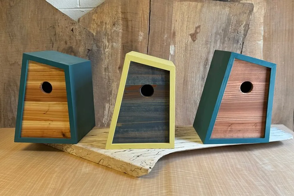 The image shows three wooden birdhouses with different color accents set against a rustic wooden background