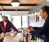 Three men are engaged in a conversation at a bar counter with one man pouring a drink from a bottle into a glass