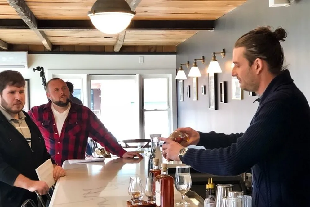 Three men are engaged in a conversation at a bar counter with one man pouring a drink from a bottle into a glass