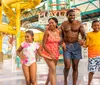 A family is joyfully running through water at a colorful water park with slides in the background
