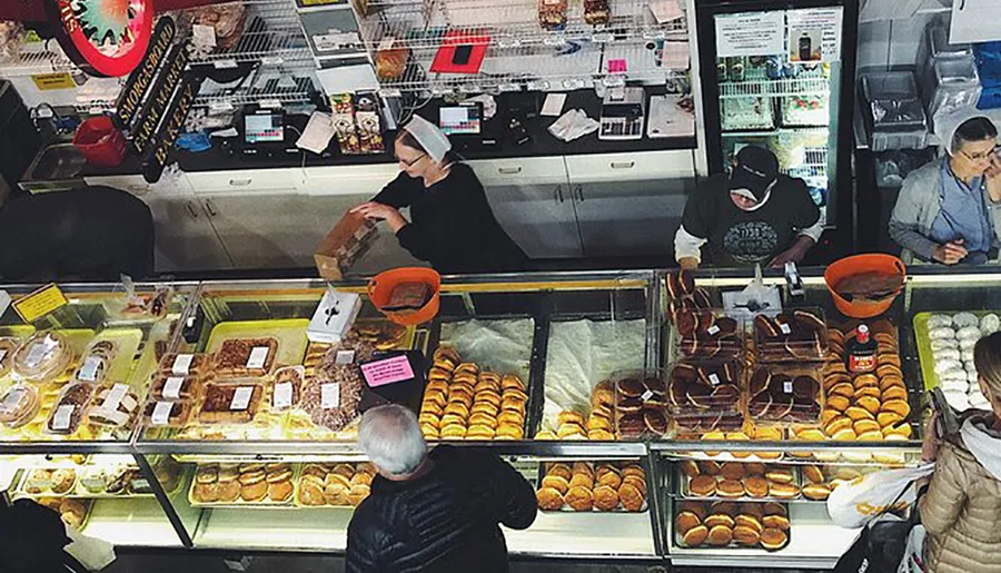 Workers are attending to customers at a bustling bakery counter filled with an assortment of bread and pastries.