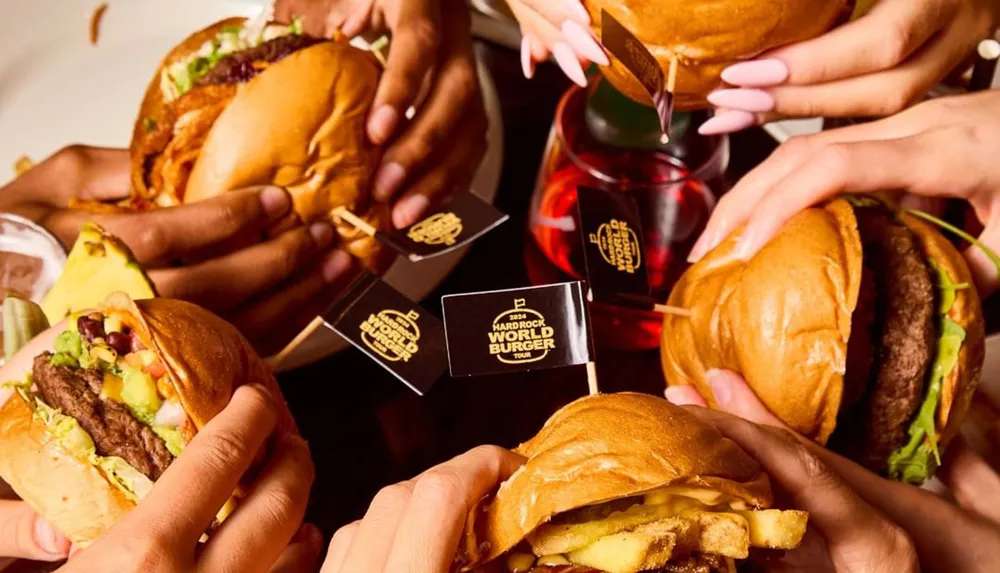 A group of peoples hands is shown holding various burgers with a label that reads Hard Rock World Burger Tour