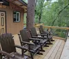 Two people are smiling and sitting on wooden chairs on the porch of a cabin surrounded by trees