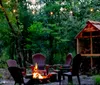 Two people are smiling and sitting on wooden chairs on the porch of a cabin surrounded by trees