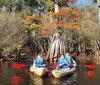 Three people are kayaking in a scenic waterway surrounded by trees with some showing autumnal colors