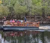 A group of people is enjoying a scenic boat tour on a calm river amidst a forested area