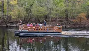 A group of people is enjoying a scenic boat tour on a calm river amidst a forested area.