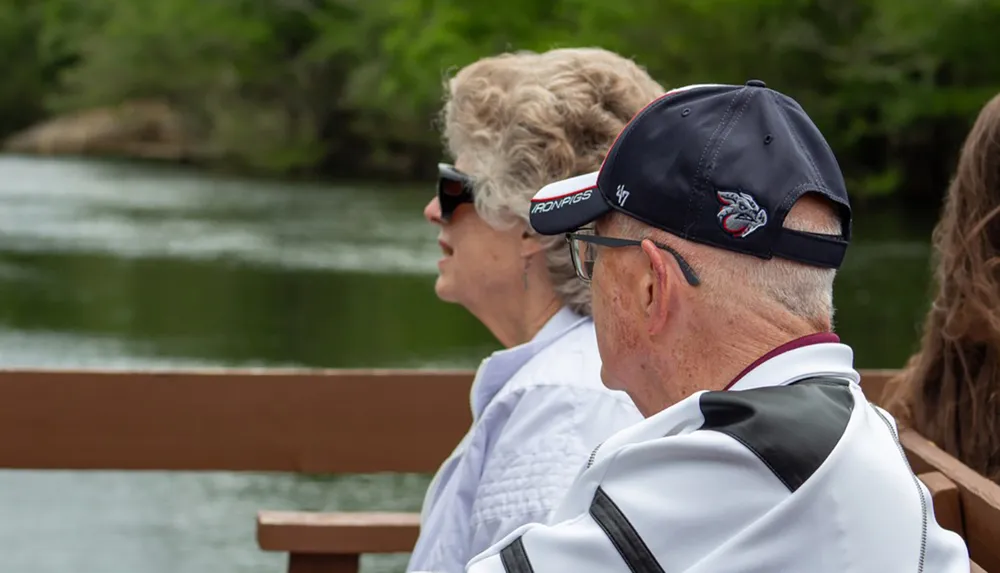 Two people are sitting and looking out over a body of water with lush greenery in the background