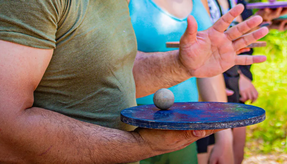 A person is attempting to balance a stone on a board gesturing with their hands open as if to show control of the object without physical contact