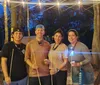 People are gathered around a campfire at twilight enjoying conversation and roasting marshmallows under a canopy of string lights