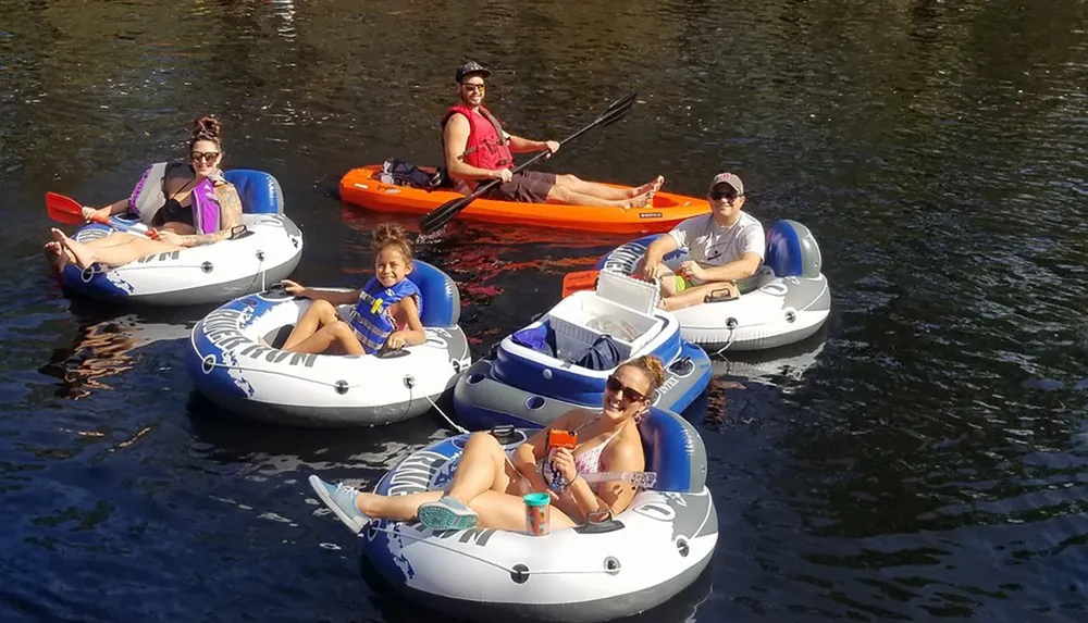 A group of people are enjoying a sunny day on the water seated in colorful inner tubes and kayaks