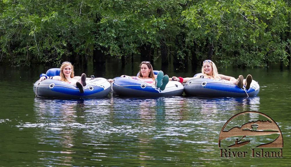 Three people are leisurely floating on a river linked together in individual blue inflatable tubes surrounded by lush greenery in what seems to be a calm and enjoyable setting