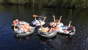 A group of people are enjoying a sunny day on the water, floating in individual inflatable rafts tied together.