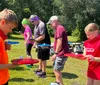 A person in a blue shirt and headband appears to be engaged in an outdoor physical activity or construction task wiping sweat from their forehead near a wooden structure with hanging ropes or straps