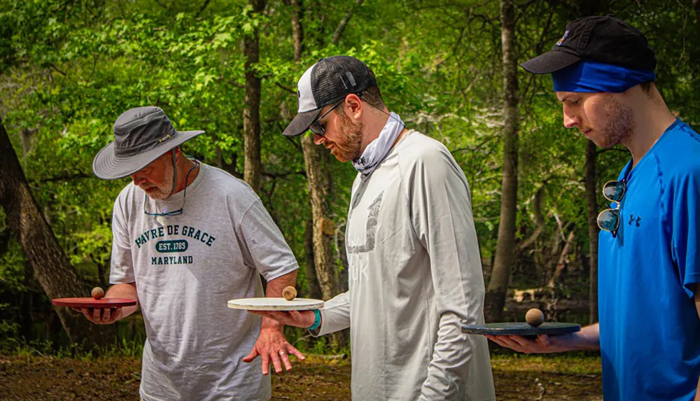 Three men are focusing intently on balancing balls on paddles in an outdoor setting