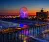 A large Ferris wheel dominates the foreground with a view of a coastal cityscape and beach in bright daylight