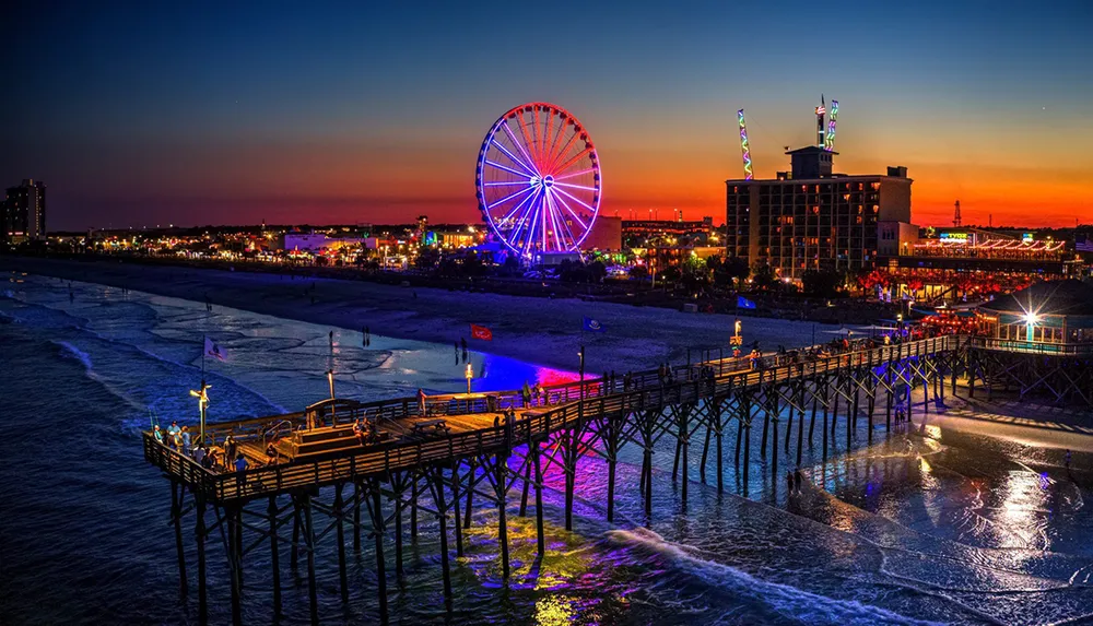 The image captures a vibrant beachfront scene at dusk with a lit-up Ferris wheel a bustling pier and a colorful twilight sky