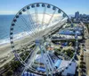 A large Ferris wheel dominates the foreground with a view of a coastal cityscape and beach in bright daylight