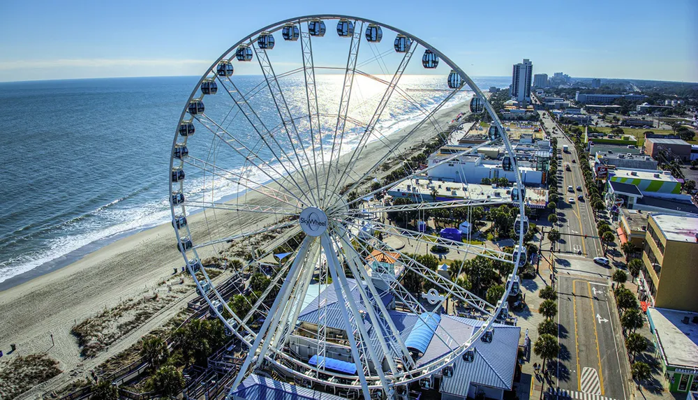 A large Ferris wheel dominates the foreground with a view of a coastal cityscape and beach in bright daylight