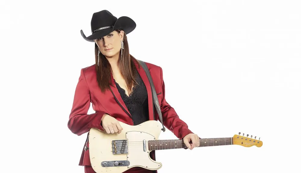 A person in a red suit and black cowboy hat is holding a cream-colored electric guitar