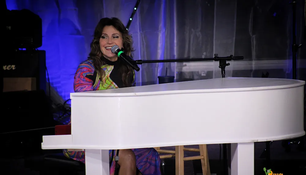 A woman is smiling and singing into a microphone while playing a white grand piano