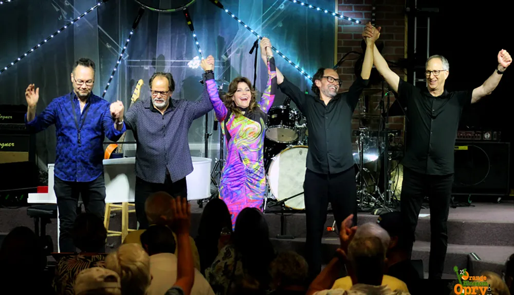 Five people on stage are holding hands and taking a bow in front of an applauding audience