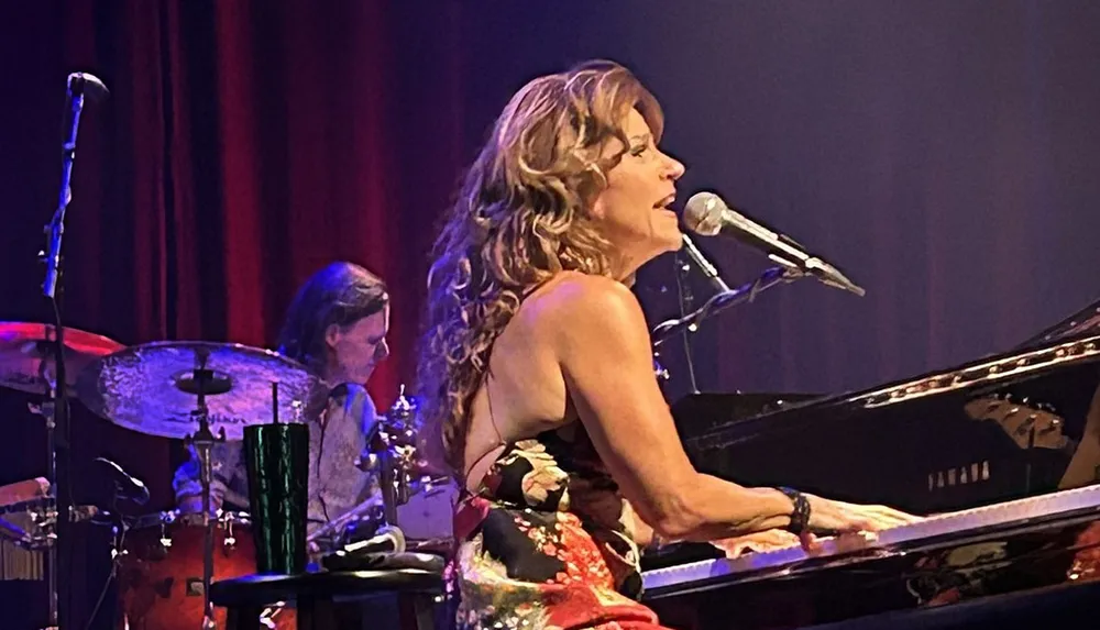 A woman is singing and playing the piano on stage accompanied by a drummer