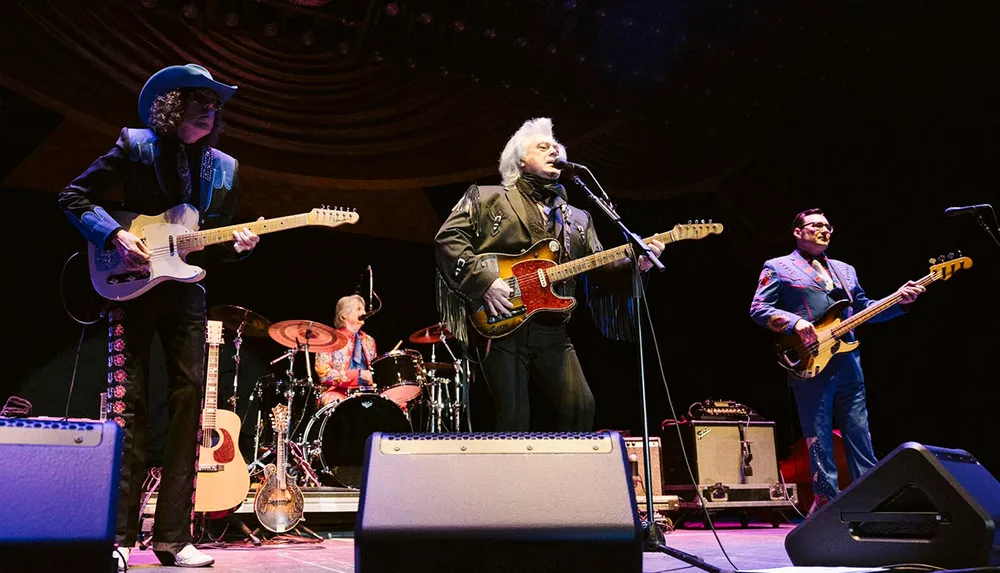 A band is performing on stage featuring a lead singer with a guitar a drummer and two other musicians playing electric guitars all dressed in colorful outfits